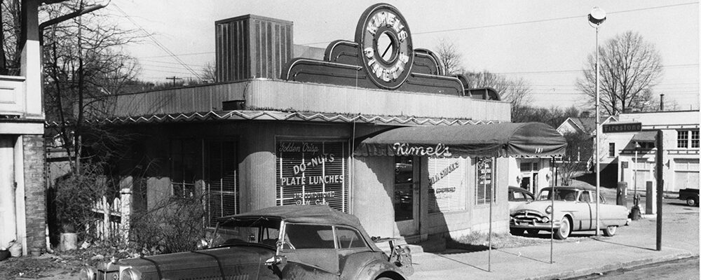 Kimel's diner, a small building with a round rooftop sign and windows advertising doughnuts and plate lunches.